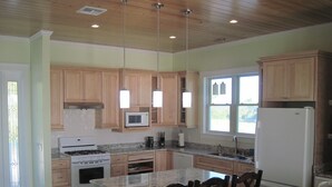 A kitchen with wooden cabinets, a white refrigerator, a stove, and a microwave. - PRIVATE LUXURY Beachfront Home, Beach Cabana, Kayaks, Paddle Board (Casuarina Point)