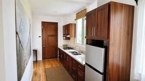 Cocina compacta con armarios de madera, refrigerador de acero inoxidable y una ventana sobre el lavamanos.
