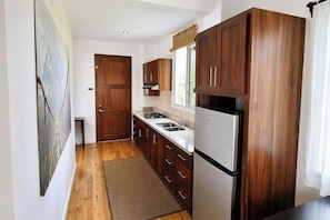 Cocina compacta con armarios de madera, refrigerador de acero inoxidable y una ventana sobre el lavamanos.