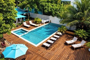 A rectangular swimming pool with a wooden deck, surrounded by lounge chairs and umbrellas. - #S4-West Bay 1 Bed Apt - 2 min walk to the beach! (West Bay)