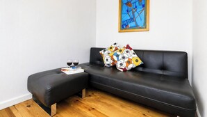 Una sala moderna con un sofá de cuero negro, un cojín colorido, dos copas de vino y una obra enmarcada en la pared.