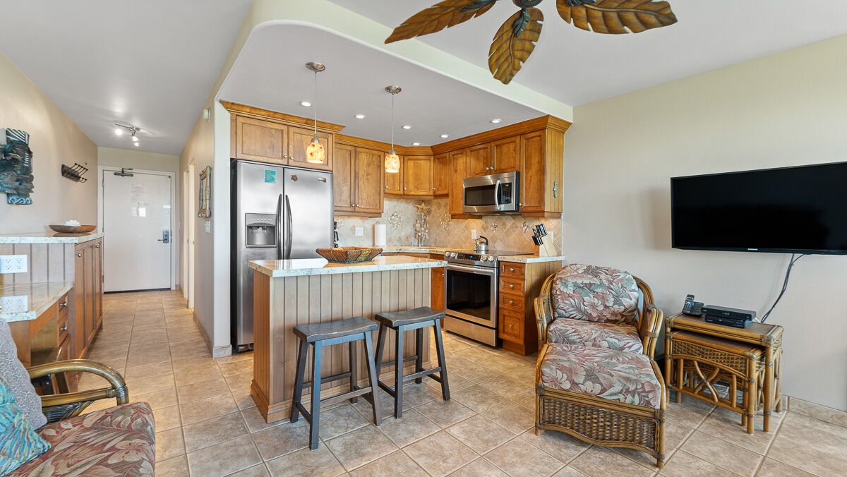 A spacious kitchen with wooden cabinets, a stainless steel refrigerator, a microwave, and a large island with stools.
