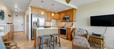 A spacious kitchen with wooden cabinets, a stainless steel refrigerator, a microwave, and a large island with stools.