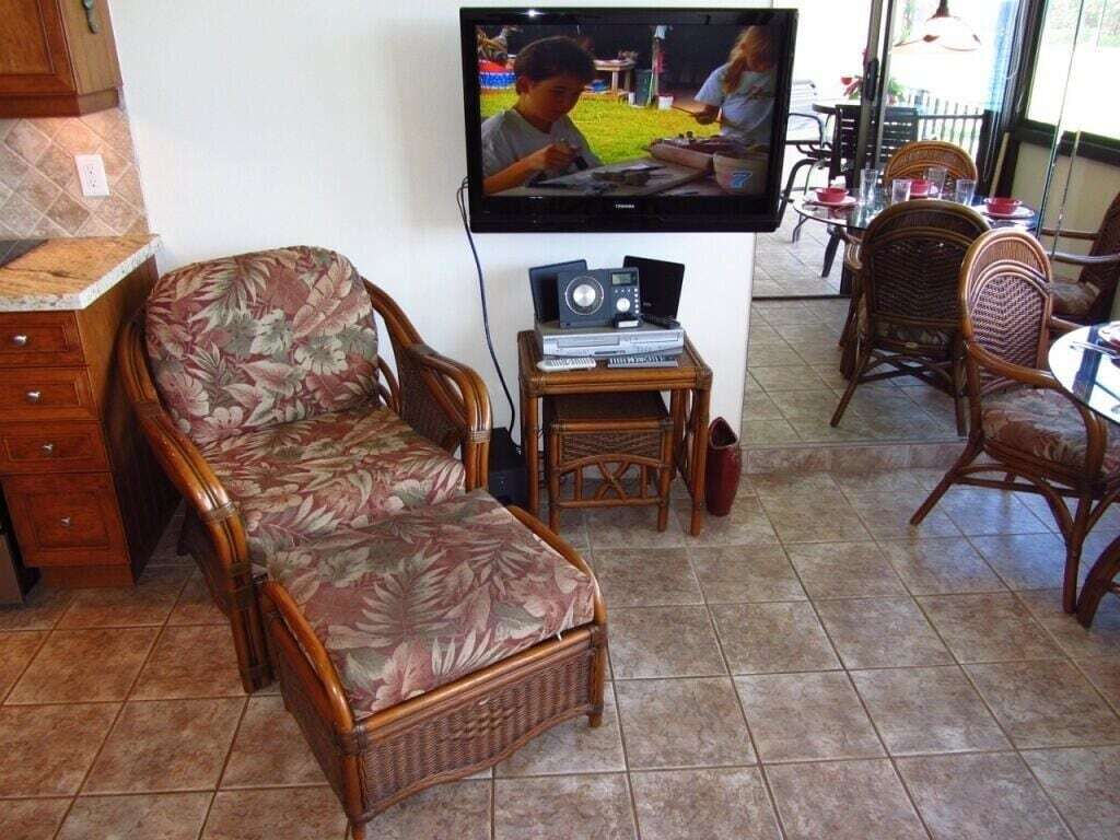 Een woonkamer met een televisie, een klein tafeltje met elektronische apparaten en rieten meubels.