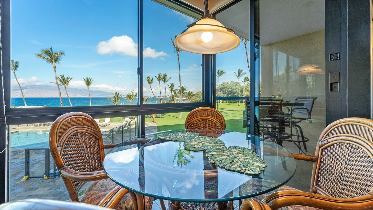 Een glazen tafel met rieten stoelen, uitzicht op de oceaan en een terras met palmbomen.