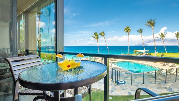 Een balkon met een glazen tafel, stoelen en uitzicht op de oceaan en palmbomen.
