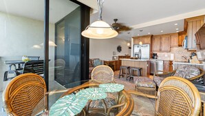 Een moderne keuken met houten kasten, een eethoek met rieten stoelen en een glazen tafel, en een schuifpui naar een balkon.