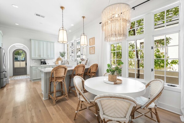A spacious kitchen with a central island, white cabinetry, and a dining area with wicker chairs.