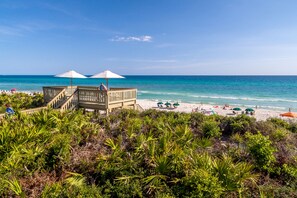 A beach with a wooden structure, beach umbrellas, and people relaxing.