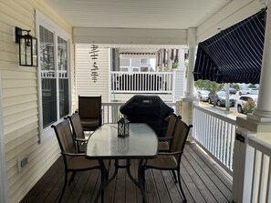 Une véranda abritée avec une table et des chaises, un barbecue et une vue sur les voitures garées.