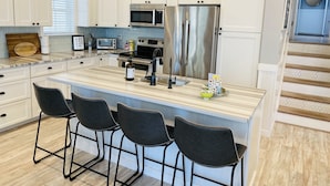 A modern kitchen with white cabinetry, stainless steel appliances, a large island with bar stools, and pendant lighting. - Amazing Location! PRIME location on Wesley.  Includes Tags/Chairs/Umbrellas!  (Ocean City)