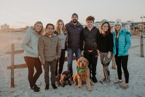 A group of people and dogs on a sandy beach with a wooden fence and buildings in the background. - Amazing Location! PRIME location on Wesley. Includes Tags/Chairs/Umbrellas! (Ocean City)