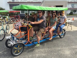 A group of people riding a three-wheeled vehicle with a green canopy. - Amazing Location! PRIME location on Wesley. Includes Tags/Chairs/Umbrellas! (Ocean City)