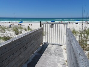 A wooden boardwalk leading to a beach with umbrellas and beach chairs.