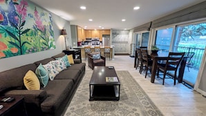 A living room with a sofa, coffee table, and a dining area with chairs and a table. There is a kitchen in the background with a stove and refrigerator. - Luxury Condo w/ FREE WiFi, Parking, Heated Pool, Hot Tubs, Skier Shuttles (Avon)