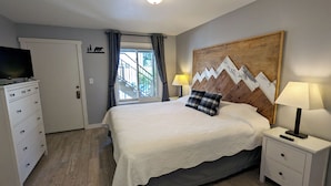 A bedroom with a bed, a nightstand, a dresser, a television on the dresser, a window with curtains, and a wall decoration. - Luxury Condo w/ FREE WiFi, Parking, Heated Pool, Hot Tubs, Skier Shuttles (Avon)