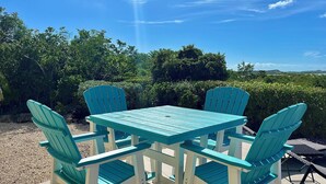 A turquoise outdoor table and chairs set on a patio with a view of greenery and hills in the background. - Escape to Westview Gardens, 3 bedroom home with private pool & sunset views. (Long Bay Hills)