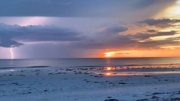Een strand met verspreide rotsen en een zonsondergang op de achtergrond.