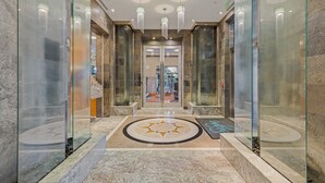 Un hall d’hôtel moderne avec un sol en marbre, des murs en verre et un espace central abritant les ascenseurs.