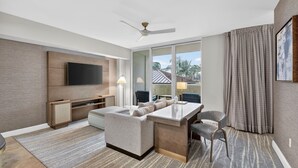Une chambre d’hôtel moderne dotée d’une télévision à écran plat, d’un canapé, d’une table à manger et offrant une vue sur les palmiers.