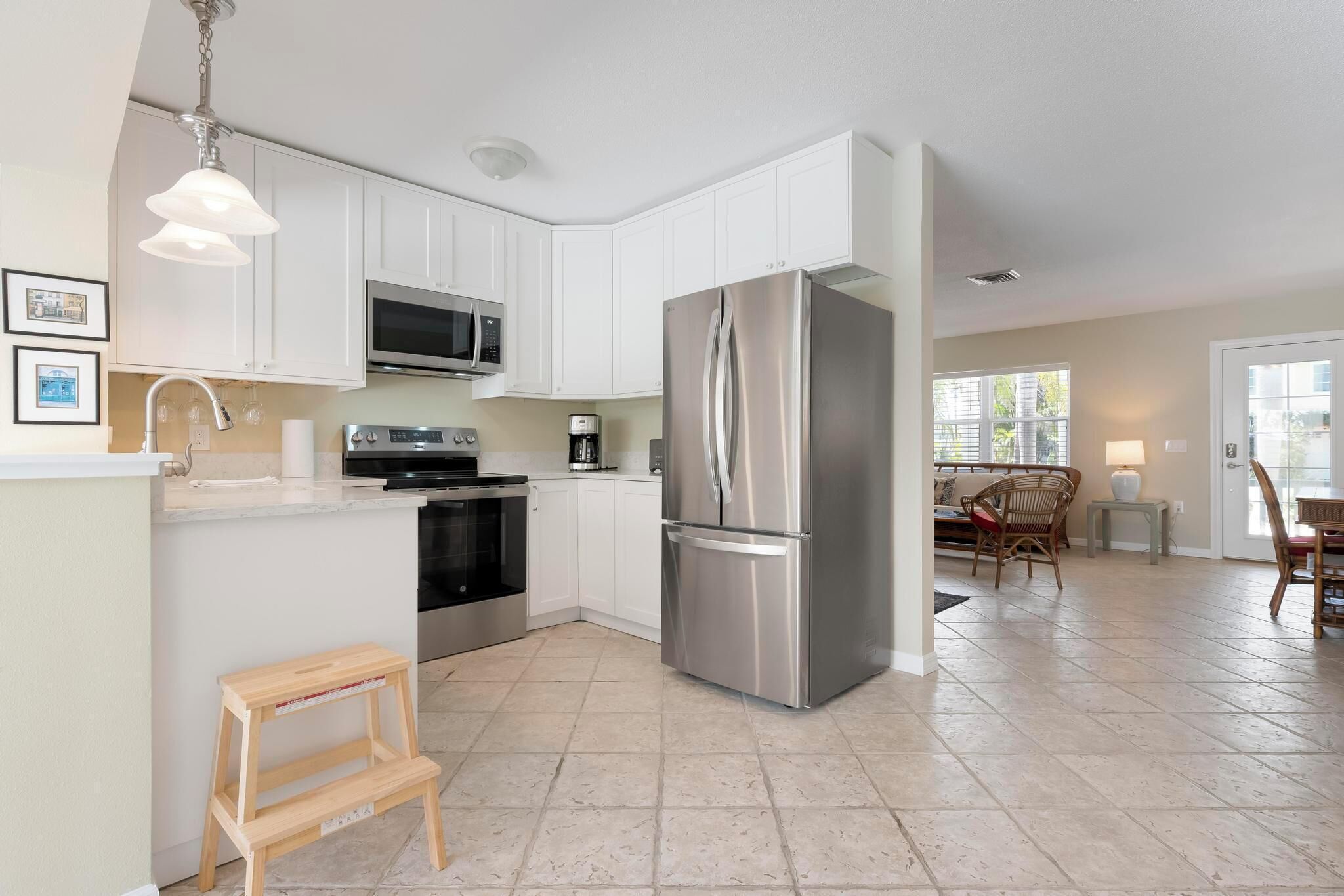 A modern kitchen with white cabinets, stainless steel appliances, a wooden stool, and a dining area with a table and chairs.