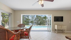 A dining area with wicker furniture and a glass table, a ceiling fan, and a view of a swimming pool. - Perfect Anna Maria. Dock on Canal - 3 blocks to sugar sand beach. Heated pool. (Anna Maria)