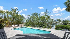 A swimming pool with a wooden deck, surrounded by lush greenery and trees. - Perfect Anna Maria. Dock on Canal - 3 blocks to sugar sand beach. Heated pool. (Anna Maria)