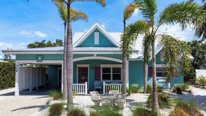 A coastal house with a porch, outdoor seating, and palm trees. - Perfect Anna Maria. Dock on Canal - 3 blocks to sugar sand beach. Heated pool. (Anna Maria)