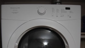 Une machine à laver Frigidaire Affinity blanche, à chargement frontal, dotée d’un panneau de commande et d’un petit mot jaune collé sur la porte.