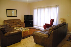Relax in this inviting living room with a sofa, coffee table, and flat-screen TV, surrounded by natural light and a comfortable armchair.