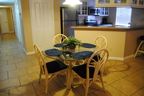 Compact kitchen with central island, refrigerator, microwave, and toaster. Dining area with glass-top table and four chairs.