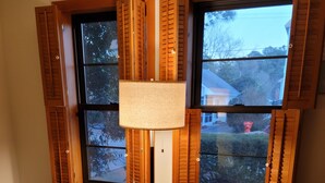 Una habitación con dos sillones iguales, una lámpara de pie y una ventana con contraventanas.