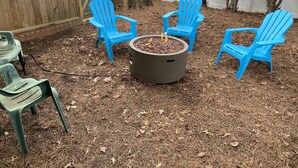 Un espacio de patio con un brasero y cuatro sillas Adirondack azules dispuestas alrededor.