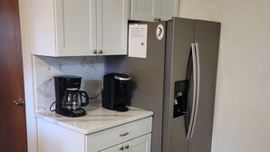 Una cocina con gabinetes blancos, un refrigerador de acero inoxidable, una cafetera y un protector contra salpicaduras de mármol.