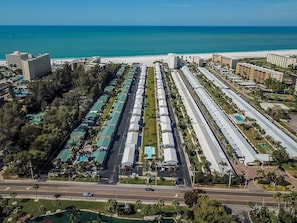 Una vista aerea di un hotel sulla costa, con diversi edifici, una spiaggia e una strada trafficata.