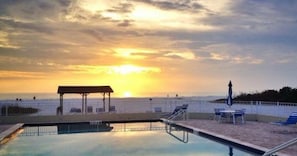 Area piscina con gazebo e poltrone prendisole, affacciata su una spiaggia al tramonto.