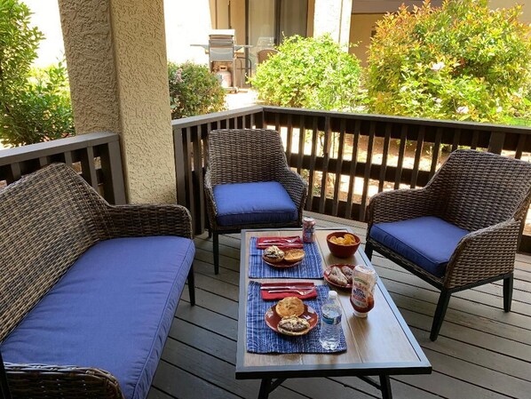 Una terraza con mobiliario de mimbre y cojines azules, una mesa dispuesta con platos, tazones y bebidas.