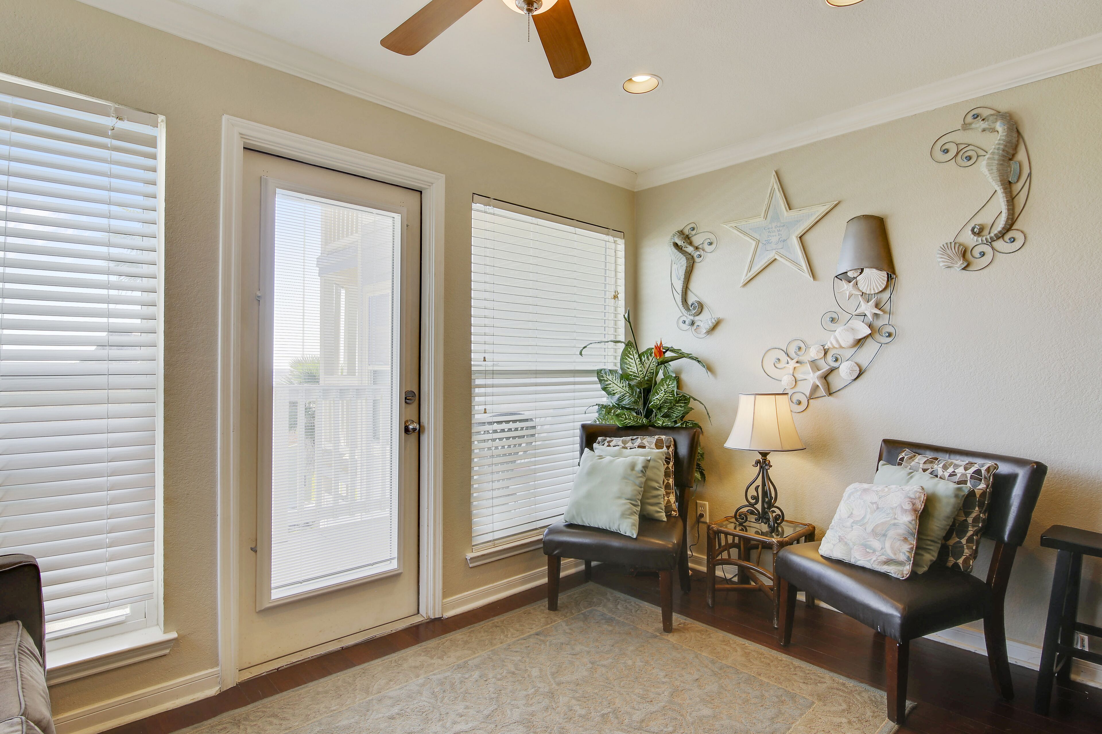 A room with two sliding glass doors, a ceiling fan, a decorative wall with a star and a plant, and two chairs with cushions.