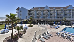 Un hotel frente a la playa con varios balcones, piscina y zonas de estar al aire libre.
