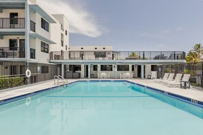 A swimming pool with lounge chairs and a building with balconies.