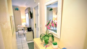 A narrow hallway with a bathroom on the right. The bathroom has a sink, mirror, and a plant. There is a door leading to another room.