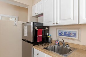 A compact kitchen with white cabinets, a stainless steel refrigerator, a sink, and a small countertop.