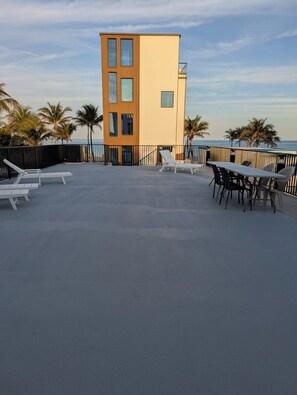 Terraza en la azotea con sillones de descanso y una mesa, con vistas al océano y palmeras.