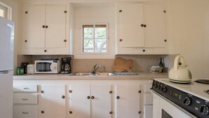 Een keuken met witte kastjes, een magnetron, een fornuis en een spoelbak.