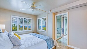 Une chambre à coucher avec un lit, un ventilateur de plafond et une vue sur l’océan par les fenêtres.