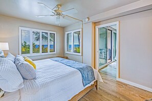 Una camera da letto con un letto, una ventola a soffitto e vista sull'oceano dalle finestre.