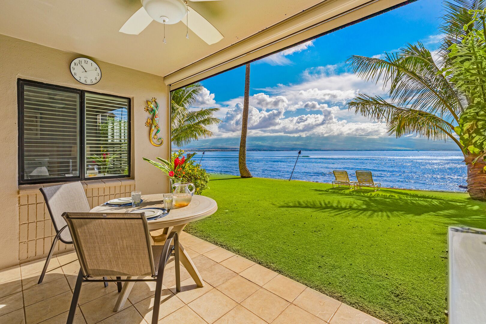 A patio with a table set for two, a clock on the wall, and a view of the ocean.