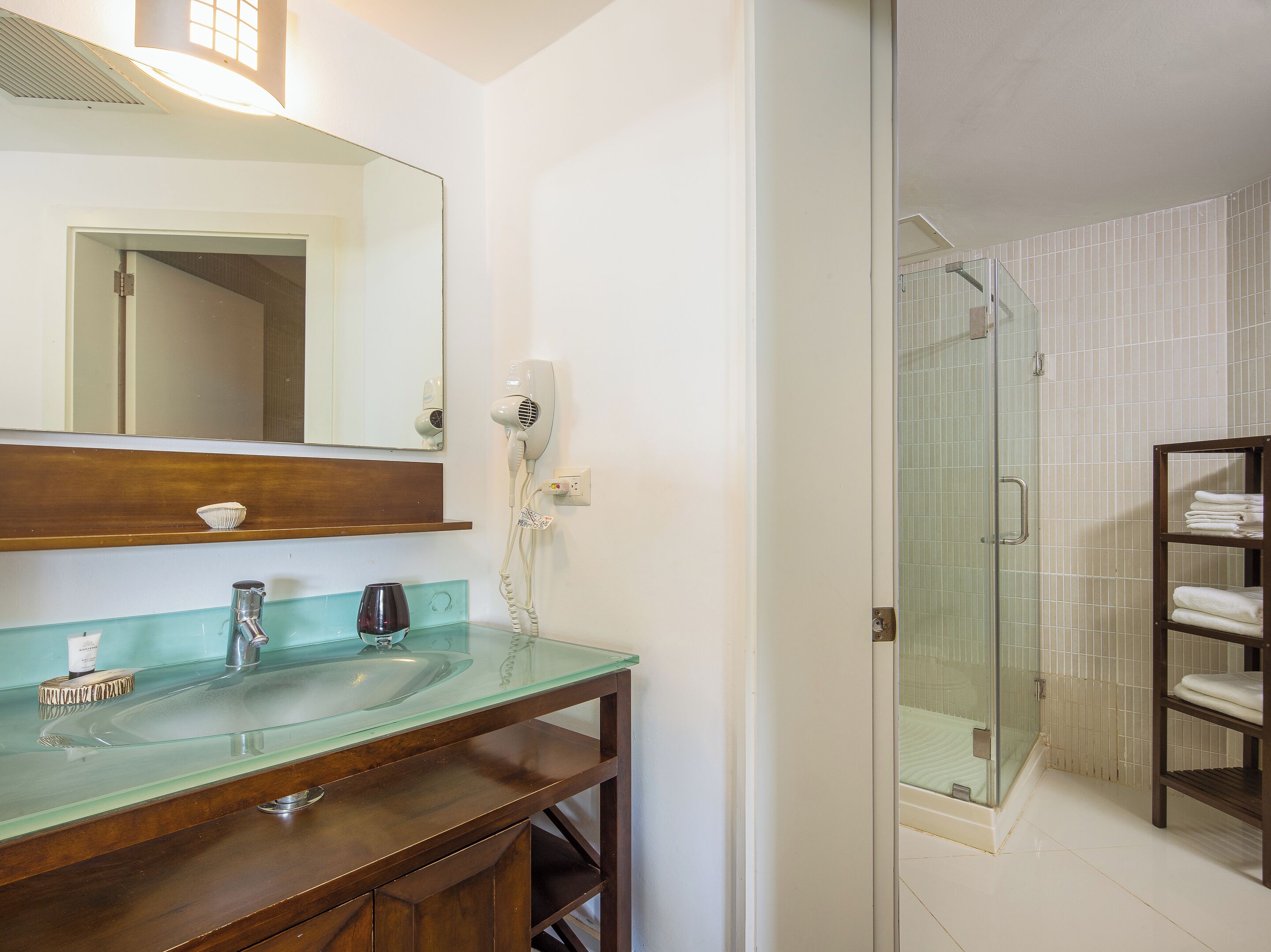 Casa de banho com lavatório de vidro, secador de cabelo e cabine de duche com vidro.