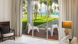 Habitación de hotel con un amplio ventanal corredera que da a una zona de piscina con sillas blancas y palmeras.
