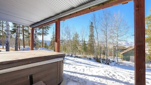 Una vasca idromassaggio in legno sotto una tettoia con vista su un paesaggio innevato e alberi.